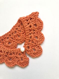 an orange crochet piece with a white bead on the end, sitting on a white surface