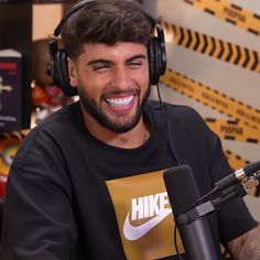 a smiling man wearing headphones sitting in front of a microphone