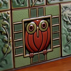 an owl is painted on the side of a wall with green and red tiles behind it