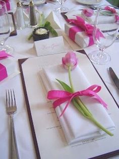 the table is set with napkins, silverware and pink tulips on them