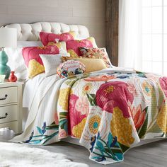 a bed with colorful pillows and blankets on top of it next to a white headboard