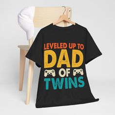 A fun t-shirt that will make a lovely, fun surprise for Father's day, birthday or Xmas. Leveled Up Dad of Twins. Available in many different colors. Production and Shipping Notes  The t-shirt is produced and shipped from Australia. Production will take 2 - 3 days. Domestic Delivery, please allow 2-7 Business Days. International Delivery, please allow 10-30 days. More about the T-Shirt Made with medium fabric (5.3 oz/yd² (180 g/m consisting of 100% cotton for year-round comfort that is sustainabl Fun Father's Day T-shirt With Graphic Print, Fun Graphic Print T-shirt For Father's Day, Father's Day Black T-shirt With Funny Print, Playful Graphic Print Tops For Father's Day, Father's Day Playful Short Sleeve T-shirt, Father's Day Letter Print T-shirt, Playful Crew Neck T-shirt For Father's Day, Black T-shirt With Lettering For Father's Day, Fun Slogan T-shirt For Gift