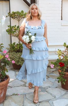 a woman in a blue dress is standing on a stone walkway with flowers and potted plants