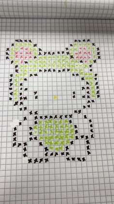 a cross stitch pattern on a piece of white paper with green and pink dots in the middle