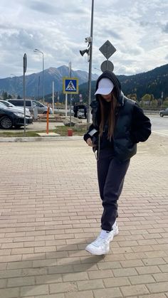 a woman in black jacket and hoodie standing on brick walkway next to parking lot