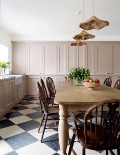 a kitchen with checkered flooring and wooden table surrounded by chairs, potted plants and hanging lights