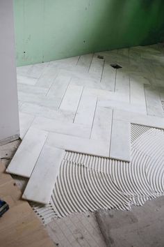 a bathroom with white tile and green walls, flooring being laid on the ground