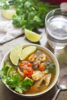 a white bowl filled with soup and garnished with cilantro, limes, tomatoes, and chicken