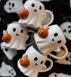 four coffee mugs with pumpkin faces on them sitting on a black and white blanket