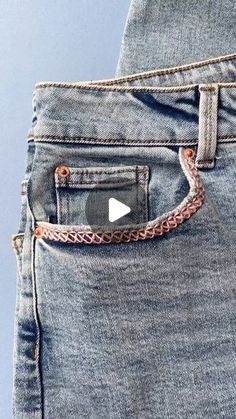 the back pocket of a pair of jeans with an orange chain on one side and a white button on the other