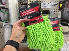 a hand holding a green dust mop in front of a store shelf with other items