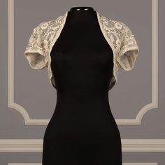 a black dress with white lace on the shoulders and back, in front of a gray wall