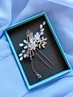 a blue box with a white flower and crystal hair pin in it's center