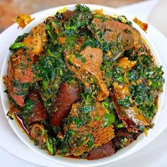 a white bowl filled with meat and greens on top of a table next to a fork