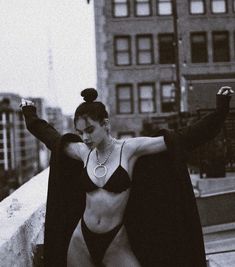 a woman in a bathing suit posing on a ledge with her arms up and legs spread out