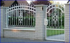 an iron gate and brick wall in front of a house with white wrought iron gates