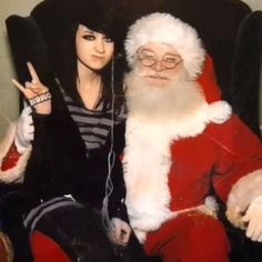 a woman sitting in a chair next to a santa clause holding a peace sign with her hand