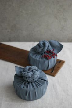 two blue bags with red beads on them sitting on a white table cloth next to a wooden board