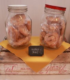 two jars filled with doughnuts sitting on top of a yellow napkin next to a wooden box