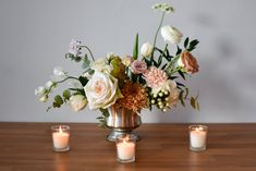 a vase filled with lots of flowers sitting on top of a wooden table next to candles