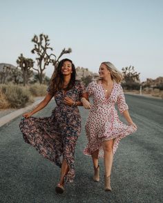 two women walking down the road in dresses and boots, one is holding her hand out