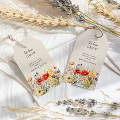 two tags with flowers on them sitting next to some dried grass and lavenders in the background