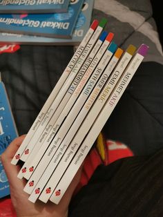 a person holding six pencils in their left hand and several books on the other