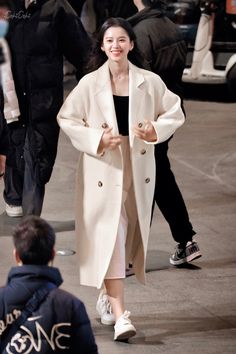 a woman walking down the street in a white coat