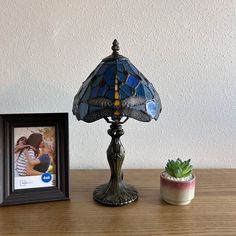 a lamp sitting on top of a wooden table next to a potted plant and framed photo