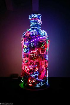 a lit up bottle sitting on top of a table next to a purple wall with writing all over it