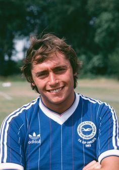 a man in a blue shirt is smiling at the camera with his arms folded out