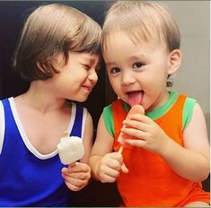 two young children sitting next to each other and eating something off of a stick in their hands