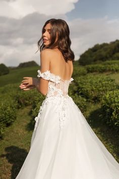 a woman in a white wedding dress is standing on the grass with her back to the camera