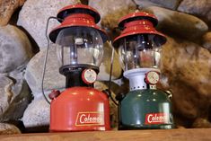 two red and green lamps sitting on top of a wooden table next to rocks in the background