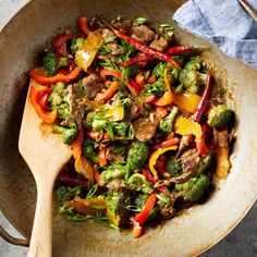 a stir fry with broccoli, peppers and meat in a wok on a table