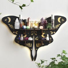 a butterfly shaped shelf with bottles and candles on it's sides, next to a plant