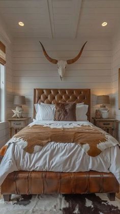 a large bed sitting in a bedroom next to two lamps and a cow head on the wall