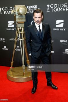 a man in a suit and tie standing on a red carpet next to an old camera