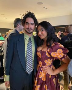 a man in a suit and tie standing next to a woman wearing a purple dress