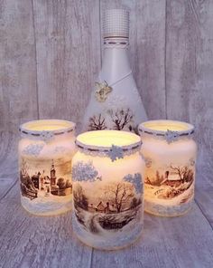 four glass jars with lit candles sitting next to each other on a wooden table near a bottle