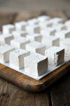 marshmallows are arranged on a cutting board with a wooden tray in the foreground