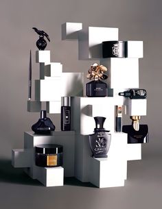 an assortment of perfumes and bottles on display in a white cubed structure with grey background