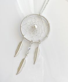 a silver dream catcher with two feathers hanging from it's side on a white surface