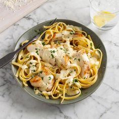 a plate of pasta with chicken and parmesan cheese on it next to a glass of water