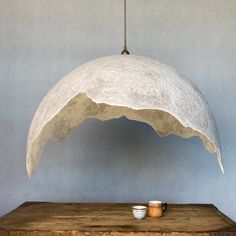 a white lamp hanging from a ceiling over a wooden table with a cup on it