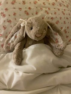 a stuffed animal sitting on top of a bed covered in white sheets and pillows with pink flowers