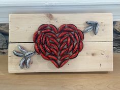 a heart made out of red beads on top of a wooden board with two silver arrows