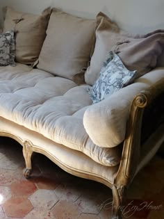 a couch with many pillows on it in front of a wall and flooring area