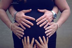 several hands on top of a pregnant woman's belly as she holds her baby bump