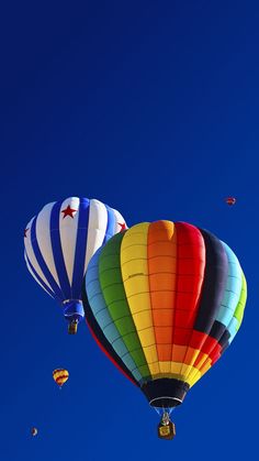 three hot air balloons flying in the sky with stars on their sides and one is red, yellow, green, blue